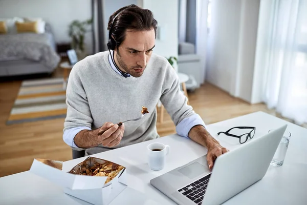 Young Freelance Worker Eating While Working Laptop Home — Stockfoto
