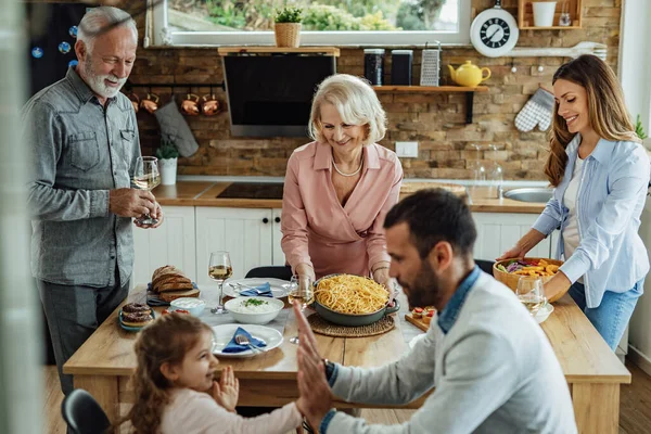 Happy extended family enjoying in a family lunch at home. Focus is on mature woman serving food at the table.