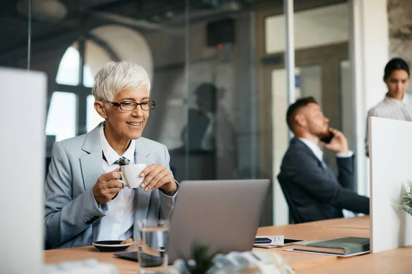 Mature Businesswoman Drinking Coffee While Reading Mail Computer Corporate Office — Zdjęcie stockowe