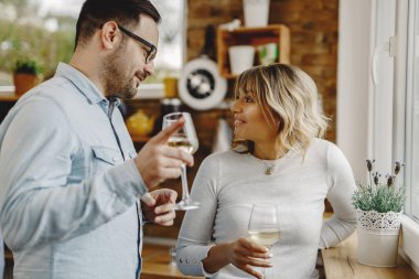 Happy couple communicating while drinking wine by the window in the kitchen. 