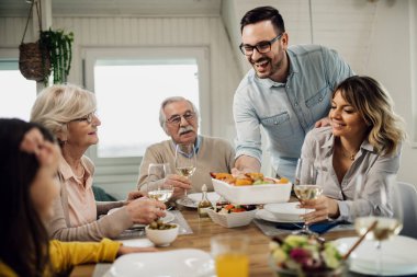 Cheerful mid adult man serving lunch to his family at dining table. 