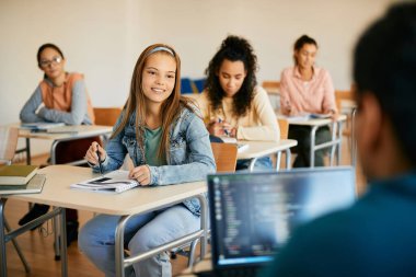 Happy teenage girl communicating with professor who is using computer during a class in the classroom.
