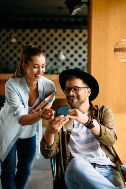 Happy university couple having fun while looking at something on smart phone in a cafe. 