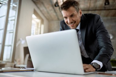 Happy entrepreneur typing an e-mail while working on laptop in the office.