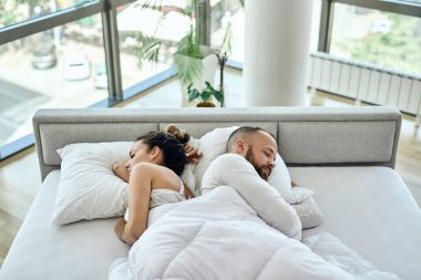 High angle view of a couple sleeping back to back on a bed. 