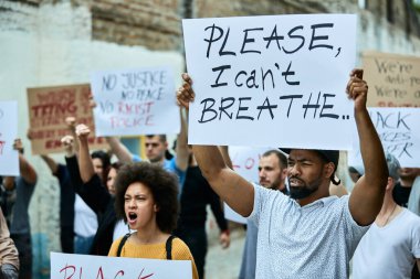 Large group of people on a Black Lives Matter protest. Focus is on black man holding a placard with Please, I can't breathe inscription. 