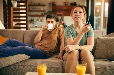 Happy woman changing channels while watching TV with her boyfriend at home.