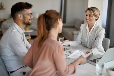 Happy financial advisor giving copies of a contract to young couple while having a meeting in the office. 