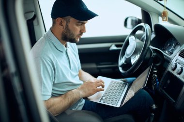Auto mechanic running diagnostic on laptop while sitting inside of a car  in a workshop. 