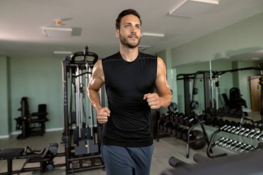 Young athletic man jogging on running track while working out in a gym.