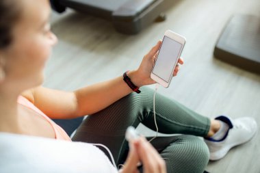 Close-up of sportswoman using smart phone while relaxing after exercising at health club. 