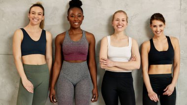 Portrait of multi-ethnic group of confident female athletes standing together against the wall and looking at camera.