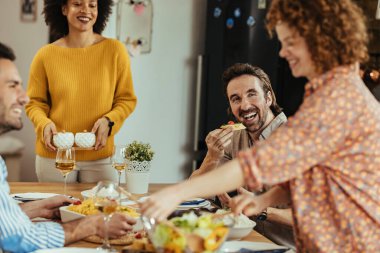 Young happy man talking with his friends and having fun while eating at dining table at home. 