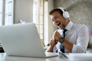 Happy entrepreneur having fun while listening music and singing in the office. 