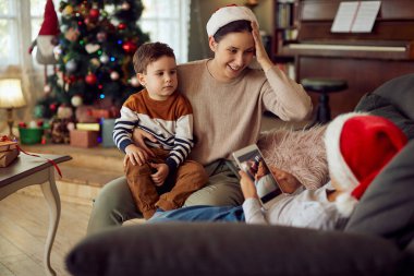 Happy mother talking to her sons while spending Christmas together at home. One of the sons is using digital tablet.
