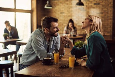 Happy man flirting with his girlfriend while holding her hand and talking in a cafe. 