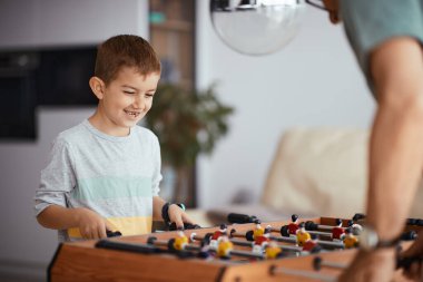 Small boy having fun with his grandfather while playing foosball together at home.