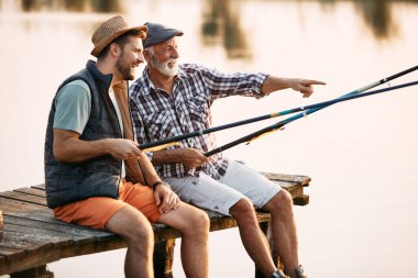 Mutlu adam tatlı suda balık tutarken babasıyla iskelede dinleniyor. Babam uzaktaki bir şeyi işaret ediyor..