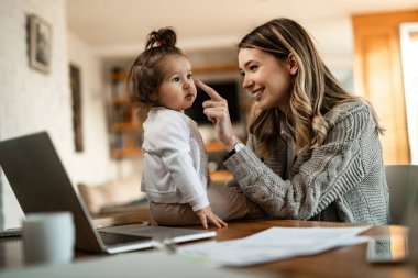 Young happy mother touching daughter nose while spending time with her at home. 