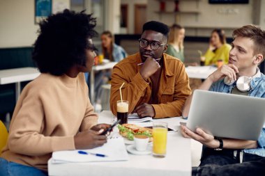 Group of multi-ethnic students learning while lunch break at university cafeteria.