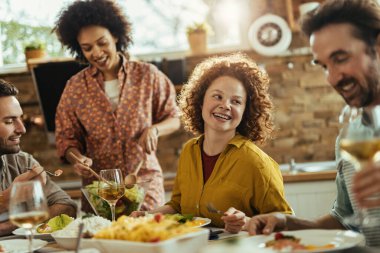 Young happy woman and her friends having lunch together at dining table. 