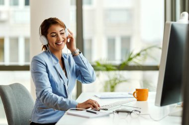 Happy businesswoman enjoying with eyes closed while listening music over headphones in the office.