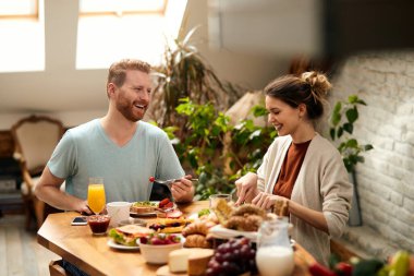 Happy couple talking while eating breakfast in dining room in the morning. 