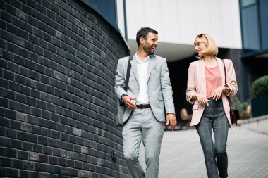 Young happy coworkers communicating while leaving office building and walking on the street. 