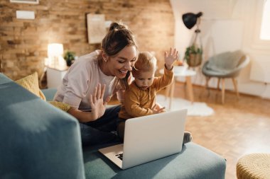 Happy mother and her small boy waving while using computer and having video call at home. 