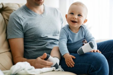 Joyful baby boy enjoying while sitting on father's lap at home. 