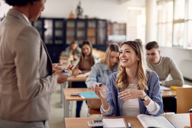 Happy college student and her professor communicating during lecture in the classroom.