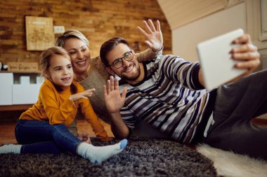 Happy family having fun while greeting someone during video call at home. 