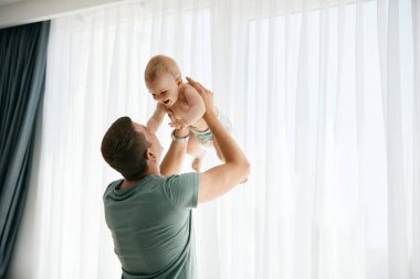Playful father having fun with his baby boy while spending time together at home. 