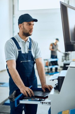 Auto mechanic using desktop PC while working in at car workshop. 