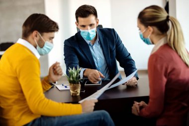 Financial advisor going through paperwork with a couple in the office and wearing face mask due to COVID-19 pandemic.