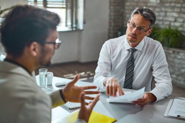 Member of human resource team talking with a candidate while reviewing his resume during job interview in the office. 