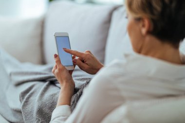 Close-up of woman relaxing at home and text messaging on mobile phone. 