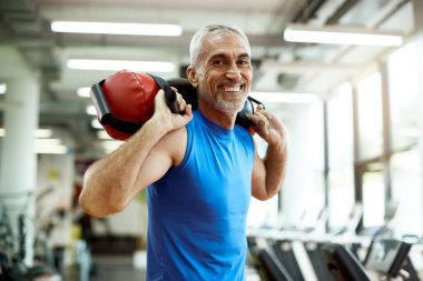 Happy mature sportsman exercises with sandbag during sports trai