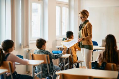 Elementary school teacher giving test results to her students in the classroom. 