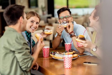 Group of happy friends eating donuts and having fun while communicating in a cafe. 