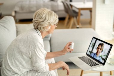 Senior woman using laptop while having video call with her doctor and talking about a medicine. 