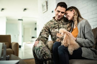 Young affectionate military couple with dog enjoying at home. 