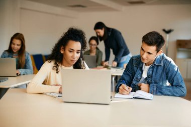 High school students writing notes while using laptop together during computer class. 