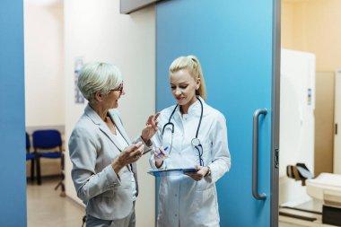 Happy doctor reading medical reports of her senior patient while talking to her in a lobby at the hospital. 