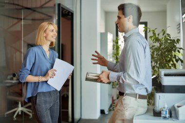 Happy coworkers communicating after printing documents on photocopier machine in the office.