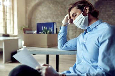 Young distraught businessman reading a notice after loosing his job due to coronavirus pandemic. 
