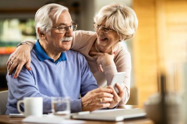 Senior man text messaging on mobile phone while wife is talking to him at home. 