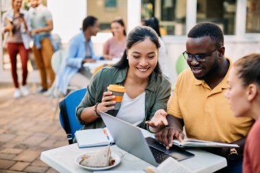 Multiracial group of friends using laptop while studying on lunch break at the university. Focus is on Asian female student. 