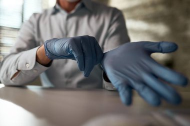 Close-up of businessman protecting his hands with gloves while working in the office during virus epidemic. 