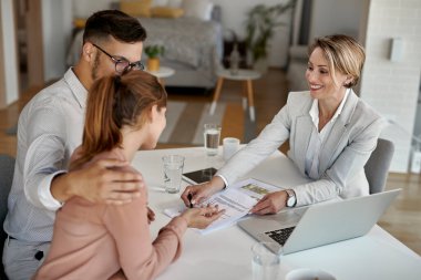Happy real estate agent offering a contract to young couple during a meeting in the office. 